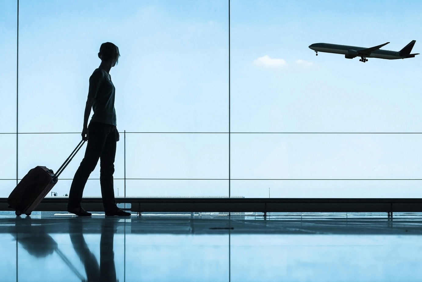 person walking with luggage at airport with airplane flying in background